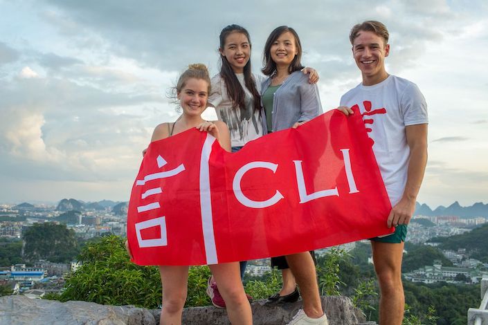 Cuatro jóvenes están al aire libre sosteniendo una bandera roja con la marca CLI impresa en ella.