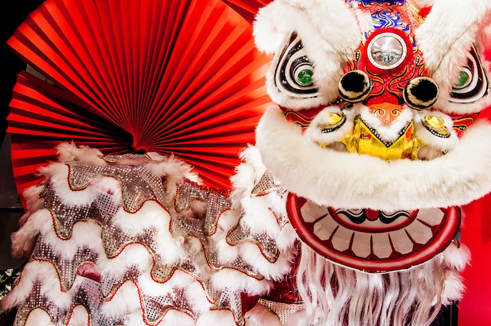 un colorido traje de danza del león chino con un abanico rojo abierto en el fondo