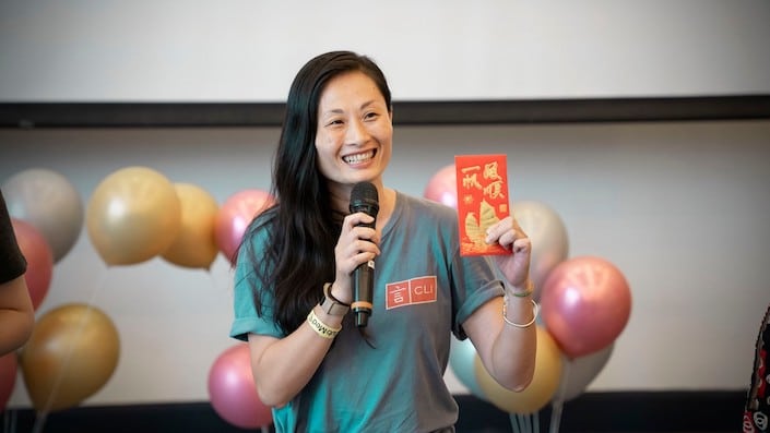 young chinese woman holding up a chinese red envelope with balloons behind her