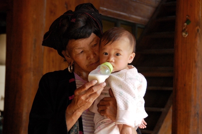 une femme chinoise de minorité ethnique en costume traditionnel donne un biberon à un bébé qu'elle tient dans ses bras