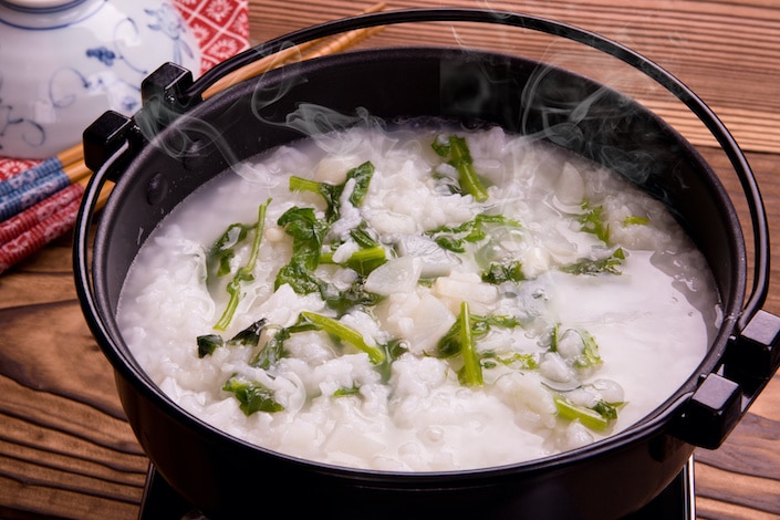 un bol de congee de riz chinois avec des légumes verts flottant dedans