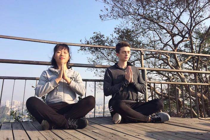 una mujer china y un hombre occidental sentados afuera junto a una barandilla meditando