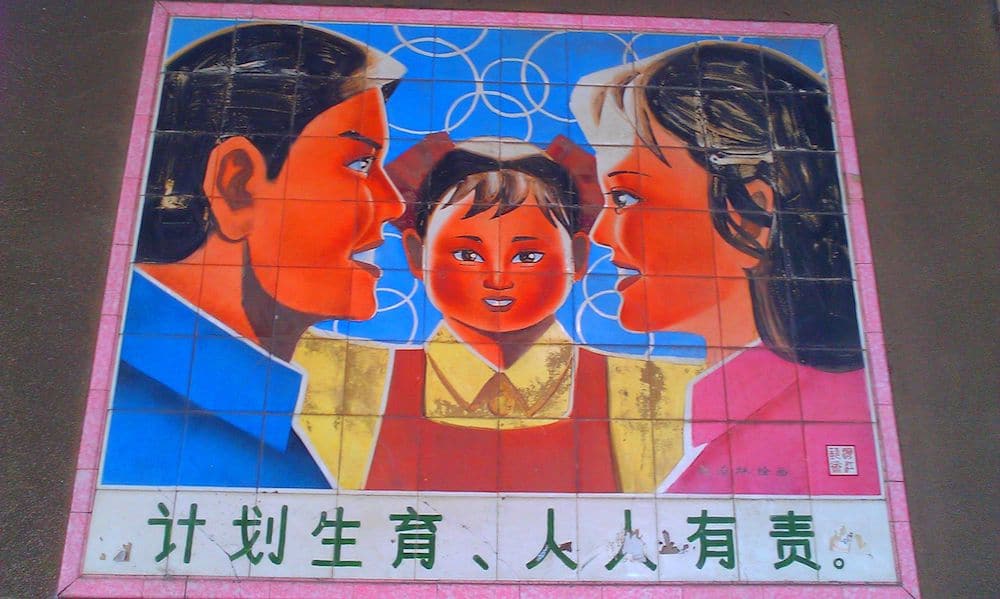 un mural de propaganda chino en color que promueve la política del hijo único que muestra a un hombre y una mujer con un hijo en el centro y con caracteres chinos en la parte inferior con la leyenda "Todos deben asumir la responsabilidad de la planificación familiar".