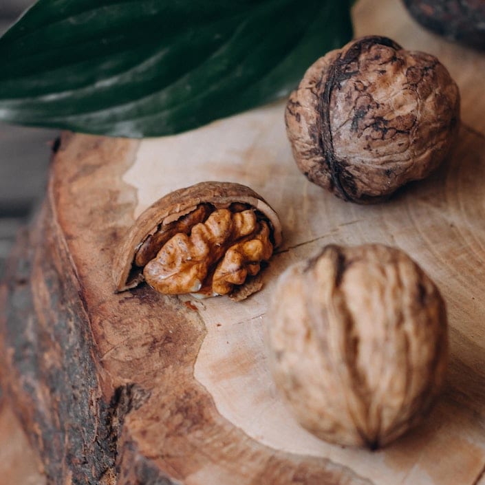 two shelled walnuts and one half unshelled walnut sitting on a piece of wood