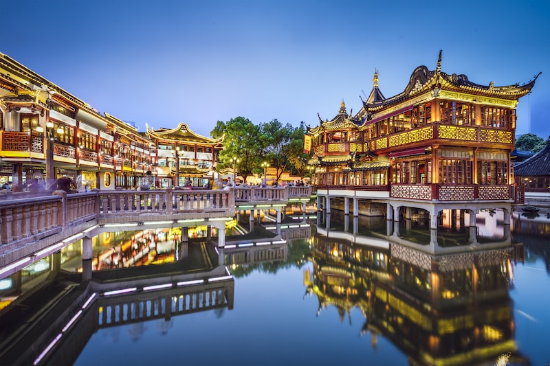 traditional Chinese buildings on stilts decorated with lights that are reflected in a lake in Yuyuan Gardens, Shanghai, China