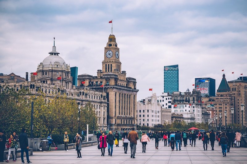 tourists walking along the Shanghai Bund with the Old HSBC building and Custom House clock tower visible in the background