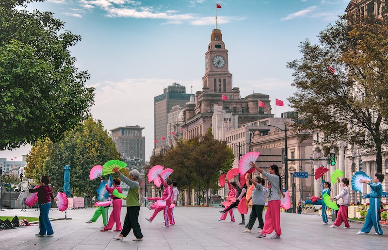 Mujeres chinas bailando con coloridos abanicos en el Bund de Shanghai con la torre del reloj Custom House en el fondo