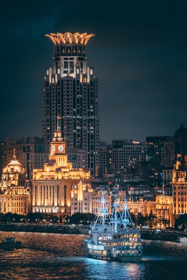 a ship on the Huangpu River at night with the Bund's Custom House clock tower in the background