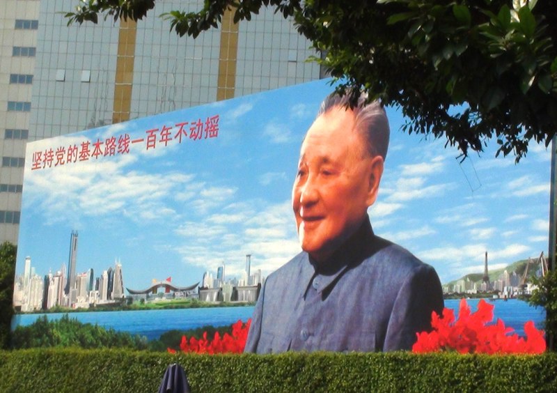 a Chinese propaganda poster featuring Deng Xiaoping with blue sky, water and skyscrapers in the background