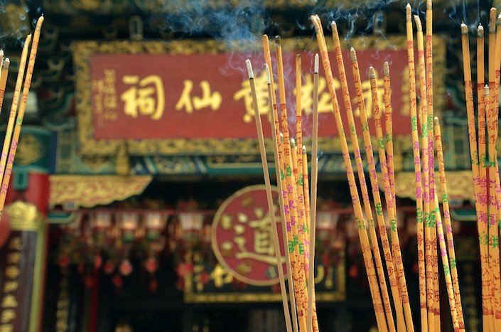 Chinese incense sticks burning in the foreground with a Chinese temple decorated with Chinese characters in the background