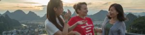 Three women laugh together with karst peaks behind at sunset