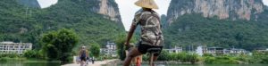 A cyclist in a conical hat rides a path toward karst peaks