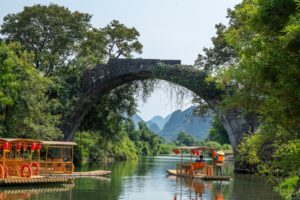 An old stone arch bridge over a river with bamboo rafts