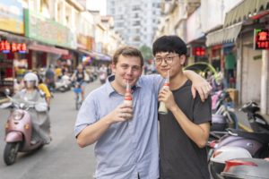Two men pose arm in arm with bottled drinks on a busy street