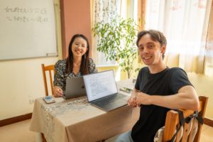 A teacher and student smile at a desk with a laptop
