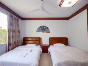 A bright room with two wooden beds and a ceiling fan