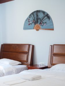 Two made beds below a fan decoration on the wall