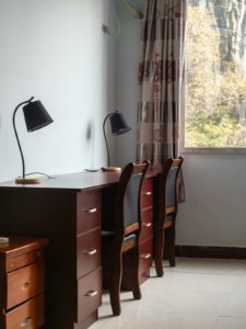 A wooden desk with a lamp beside a window