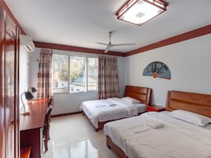 A bright twin room with beds, a desk and a ceiling fan