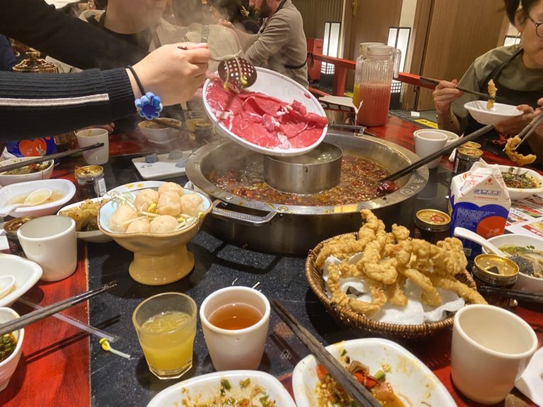 Une table dressée pour une fondue chinoise, avec des assiettes de viande et des accompagnements