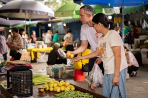 A man and a woman pick out fruit at an outdoor market stall