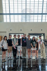 A group poses for a photo in a bright hall under a glass roof