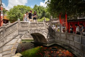 People cross a stone arch bridge over a koi pond