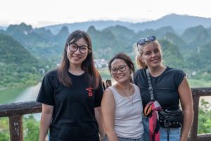 Three women smile at a viewpoint above karst hills and a river