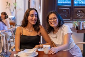 Two smiling women sit at a restaurant table with tea cups