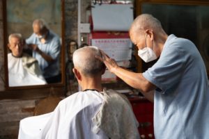 A barber in a face mask trims a man's hair, seen in a mirror