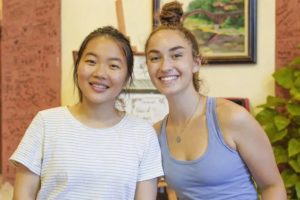 Two smiling women pose close together indoors