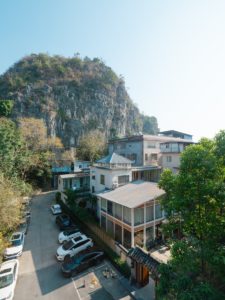 A karst hill towers over white houses with balconies and a parking lane