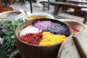 A bowl of five-colored glutinous rice beside fresh herbs and spice bowls
