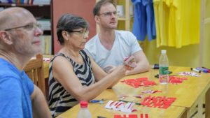 Three people cut red paper designs at a classroom table