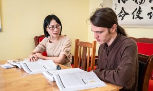 A teacher and student read from open textbooks at a wooden desk