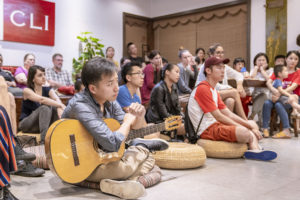 An audience on chairs and floor cushions watches a guitarist at the CLI Center