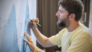 A bearded man writes a message on a painted wall
