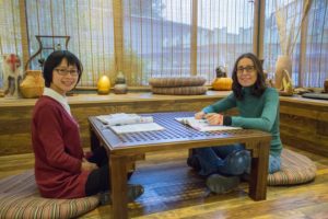 A teacher and student sit on floor cushions at a low table in a tea room