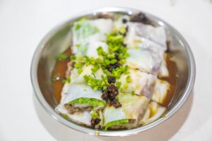 A bowl of rice noodle rolls topped with scallions and sauce
