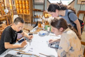 A teacher and students work on calligraphy around a crowded table