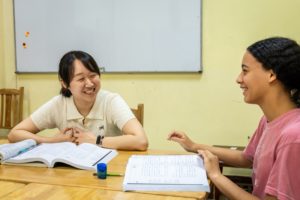A teacher and student laugh together across a classroom table