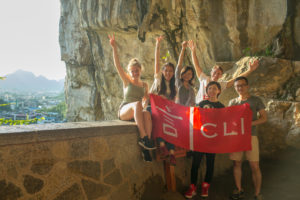 A group cheers with a red CLI banner on a cave balcony