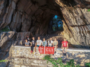 A group sits with a red CLI banner at the mouth of a huge cave