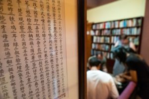 A wall of Chinese characters with people reading by a bookshelf behind