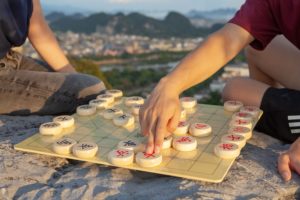 Hands move pieces on a Chinese chessboard above a hilltop city view