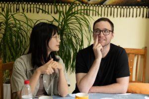 Two people sit at a table, one resting his chin on his hand in thought