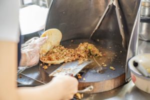 A street vendor chops filling for buns on a griddle