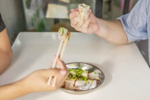 Hands use chopsticks to share food from a metal plate