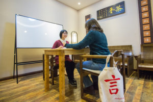 A teacher and student sit at a table beside a whiteboard