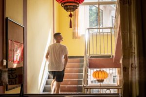 A man walks up a sunlit staircase hung with red lanterns